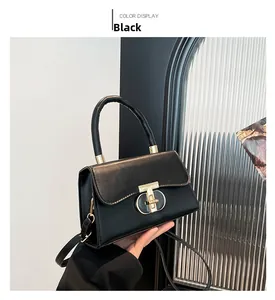 Detail of black faux leather handbag showing golden T-shaped twist lock and thick top handle