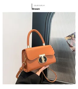 Detail of a brown leather crossbody bag with a distinctive golden T-shaped metal lock
