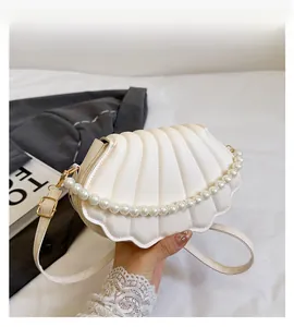 Detail view of cream shell crossbody bag with pearl handle and textured pleats