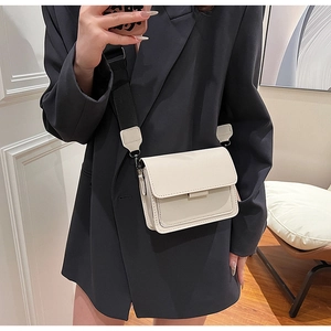 Close-up of off-white retro crossbody bag with contrast black wide strap on model