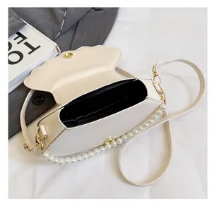 Detail of minimalist cream shell-shaped crossbody bag with pearl handle and interior view
