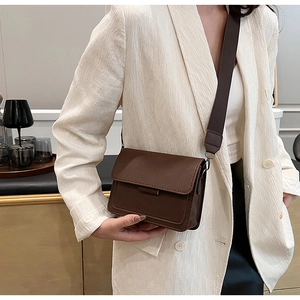 Detail of a vintage dark brown leather crossbody bag with a wide strap on a white blazer