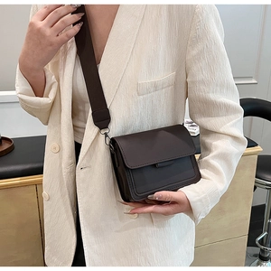 Detail of dark brown matte leather crossbody bag featuring wide fabric strap and fine stitching