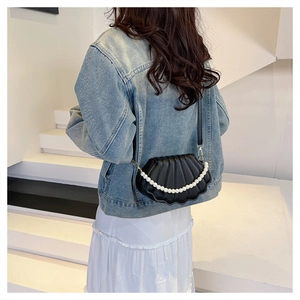 Model wearing black shell crossbody bag with pearl strap and textured pleat design