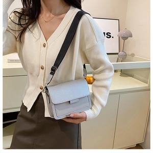 Detail of grey crossbody bag with wide black strap on a model wearing white cardigan
