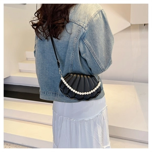 Detail of black shell-shaped crossbody bag featuring textured surface and pearl strap decor