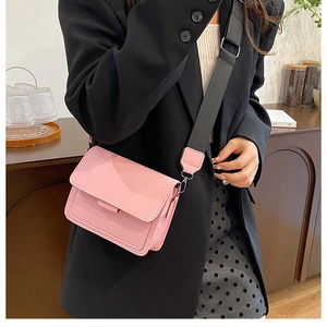 Detail of pink leather crossbody bag featuring a wide black woven strap and flap closure