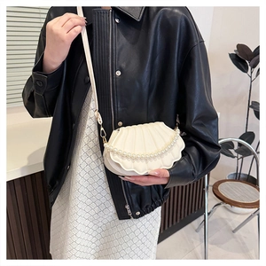 Detail of shell-shaped crossbody bag with pearl chain and wavy texture on black jacket