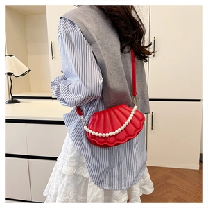 Detail of red shell-shaped bag featuring glossy texture and elegant pearl handle strap