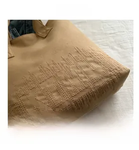 Close-up of tan canvas tote bag showing wavy embroidery stitching and fabric texture