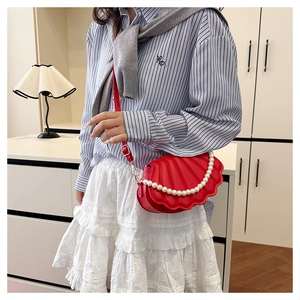 Detail of red shell-shaped crossbody bag featuring pearl handle and textured finish