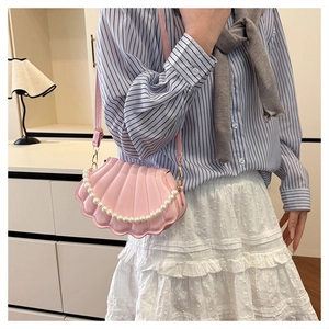 Close-up of pink shell-shaped crossbody bag with white pearl chain and textured finish