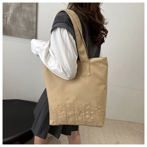Détail du sac cabas en toile kaki avec broderie TEMU porté à l'épaule par le mannequin