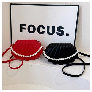Detail view of red and black shell-shaped leather bags with pearl chain accents