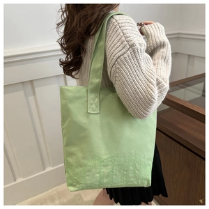 Détail du sac cabas en toile vert clair avec logo brodé et larges bandoulières