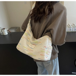 Detailed texture of off-white canvas shoulder bag with colorful embroidery and woven brand label