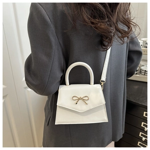 Detail of white mini bag with golden bow clasp worn by model in grey blazer