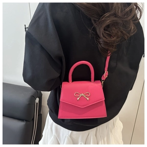 Fuchsia crossbody bag detail featuring a golden bow buckle on a smooth leather flap