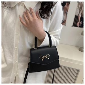 Detail of black mini crossbody bag featuring a gold bow clasp and sleek matte leather finish