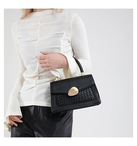 Détail d'un sac à main noir motif crocodile avec un fermoir doré géométrique élégant