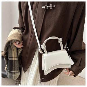 White hourglass PU leather bag with knotted handle and curved base on a wool coat