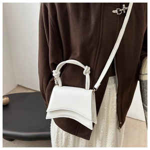 Detail view of the curved base and decorative knotted handle on this white crossbody bag