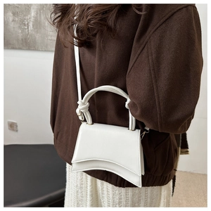 Minimalist white patent leather crossbody bag with curved base and knot handle detail