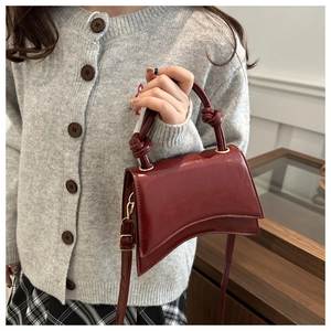 Detail of burgundy patent leather bag showing asymmetric base and knotted handle texture