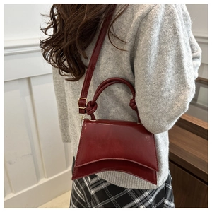 Detail of burgundy hourglass handbag with curved base and knot handle on model