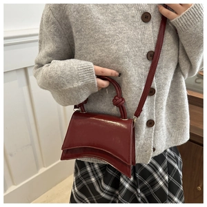 Model wearing dark red glossy leather crossbody bag with knot handle and curved base