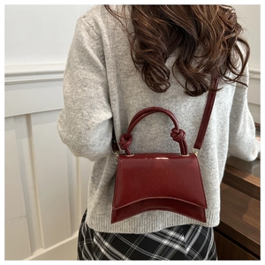 Detail shot of a wine red hourglass bag with knotted handle and glossy patent leather