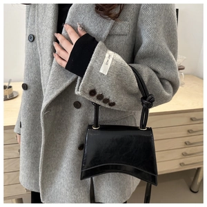 Glossy black patent leather bag with curved base shown with a grey coat outfit