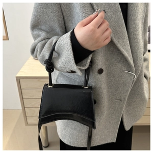 Detail of a black patent leather handbag with a unique curved bottom and knotted handle grip