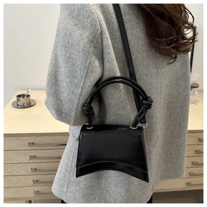 Close-up of black patent leather hourglass bag with unique knotted handle design