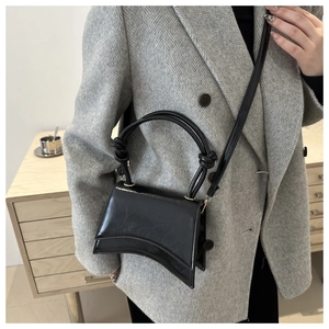 Detail of glossy black handbag with a unique curved base and sleek knot handle design