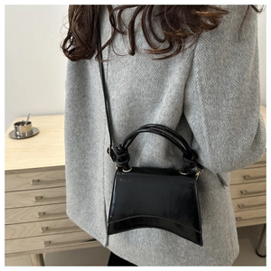 Detail of black glossy patent leather crossbody bag with a unique knot handle design