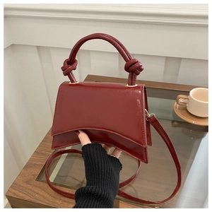 Detail of burgundy patent leather handbag featuring unique knot accents and glossy finish