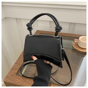 Detail of glossy black patent leather bag featuring a unique knotted handle and curved base