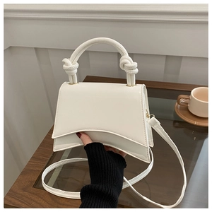 Detail of white structured bag with unique curved base and knotted handle on wooden table