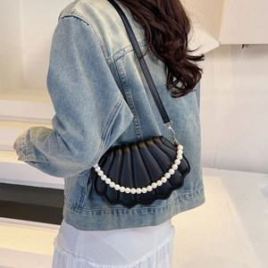 Fashionable black shell crossbody bag with pearl strap worn by model on white background