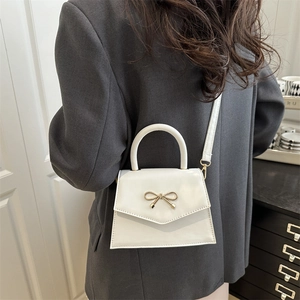 White mini trapezoid handbag with gold bow charm and detachable shoulder strap on model