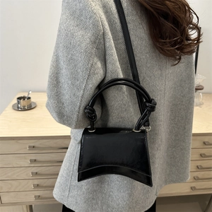 Fashionable black patent leather shoulder bag with curved base and knot handle detail