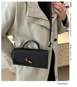 Detail of black woven leather handbag with gold knot clasp worn with a beige coat