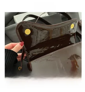 Detail of high-gloss dark brown patent leather bag showing golden magnetic buckle closure