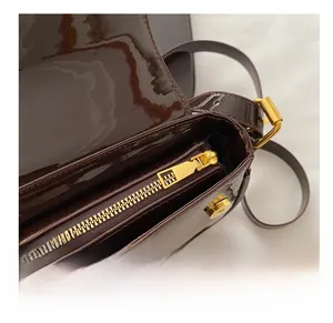 Detail of high-gloss dark brown patent leather bag with a premium golden metal zipper