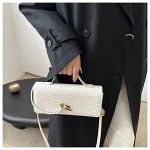 Detailed view of white woven crossbody bag with artistic gold twist lock on black coat