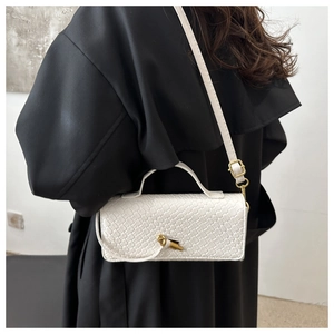 Detail of white crocodile embossed texture on crossbody bag with gold knot buckle closure