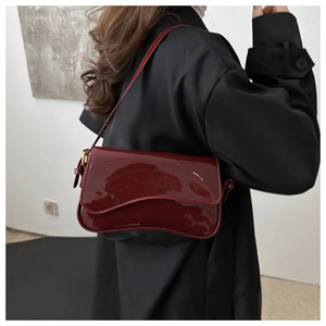 Side view of dark red patent leather shoulder bag worn over a black trench coat