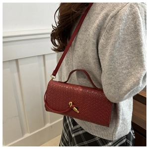 Detail of red woven crossbody bag featuring a gold twist-lock clasp and slim strap
