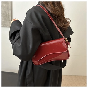 Close-up of a burgundy glossy patent leather shoulder bag with sleek curved flap design
